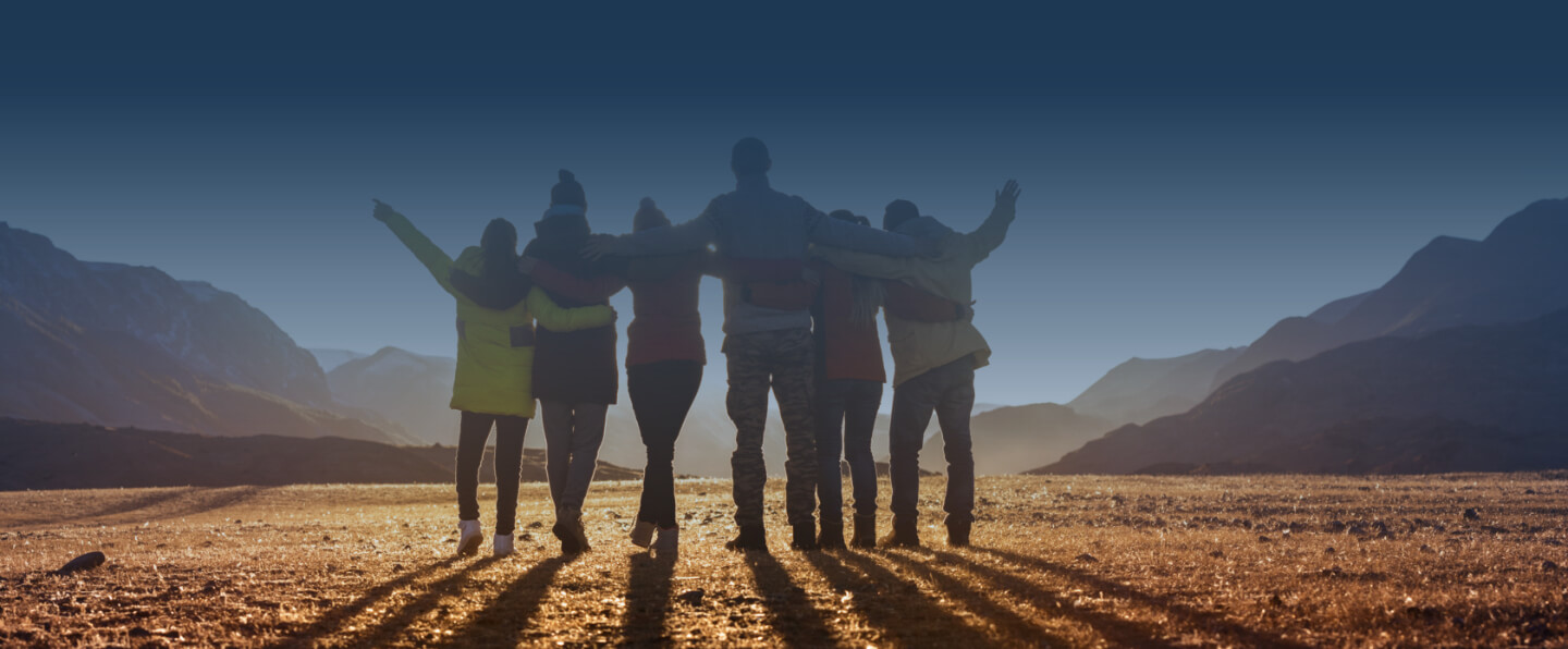 Group of people watch sunrise with arms around each other.